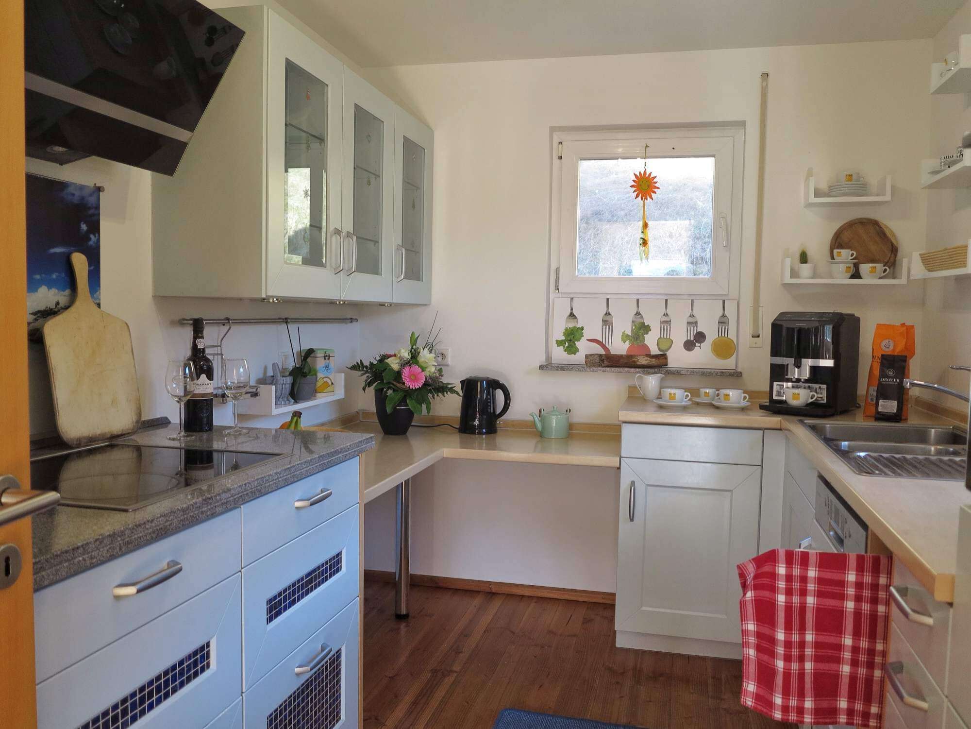 A kitchen with white cabinets, a coffee machine, a sink, and a window with a sun decoration.