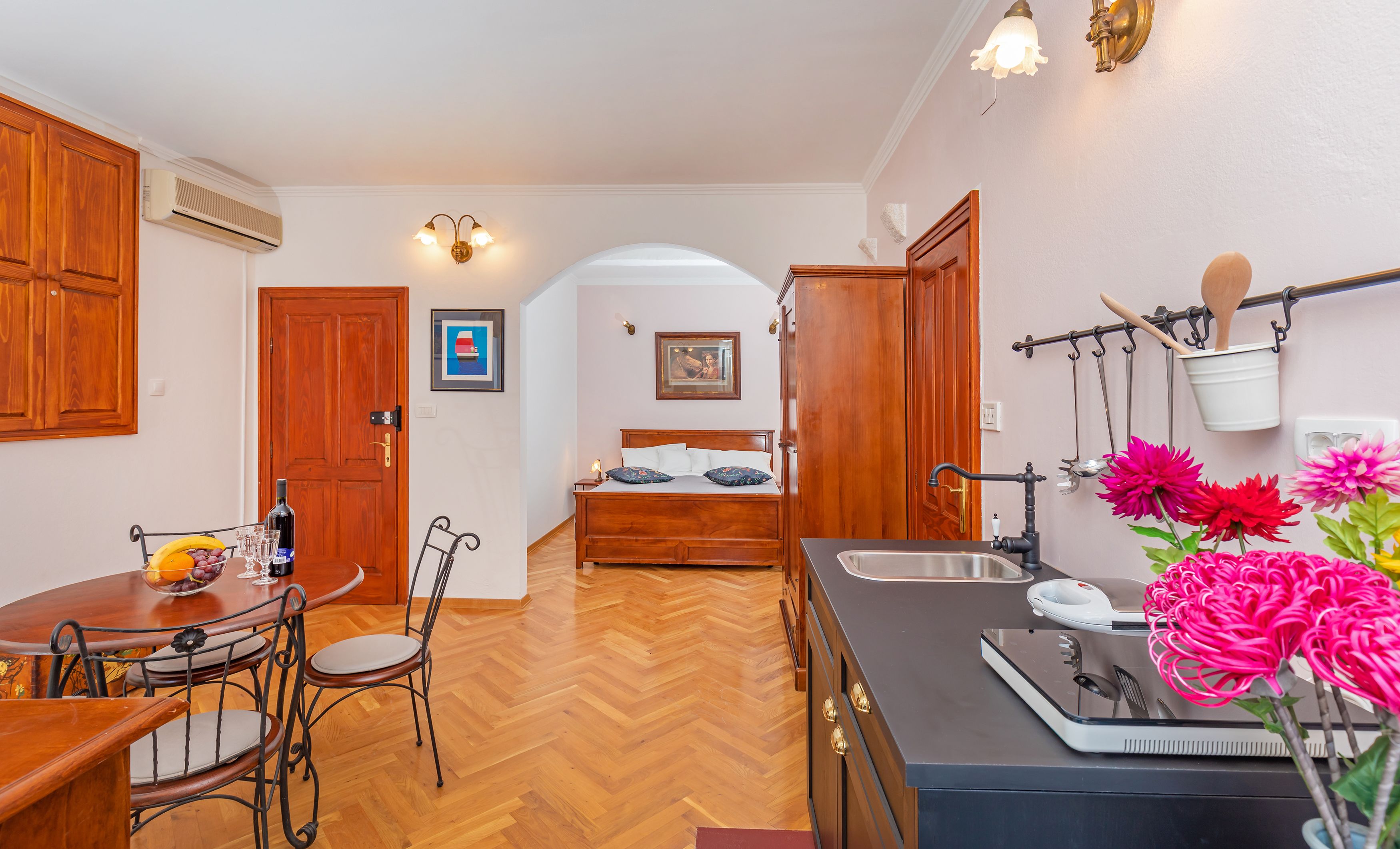 A compact kitchen with a dining area, a bed with a headboard, and a small bathroom.