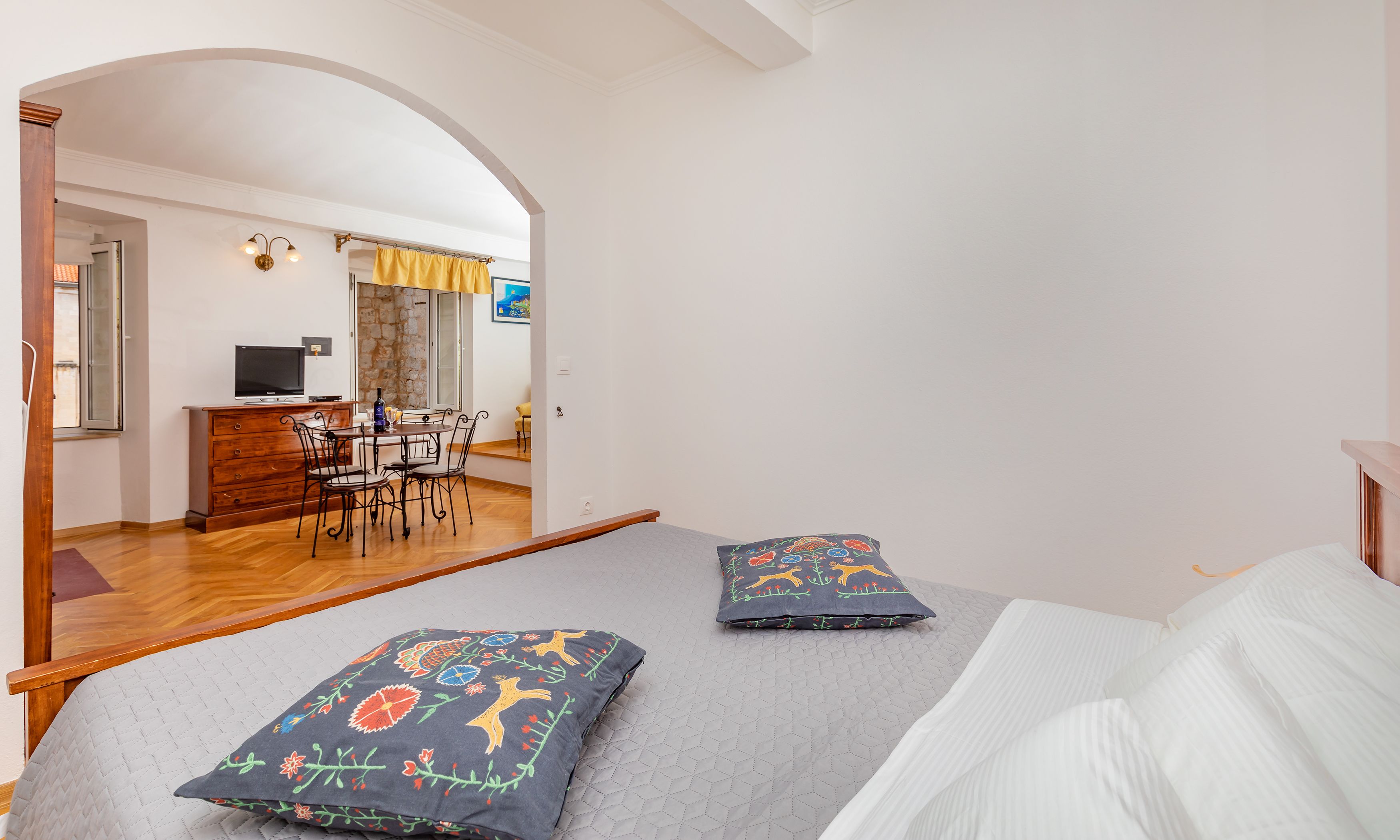 A bedroom with a bed, two pillows, a desk with a chair, a television, and a dining table.