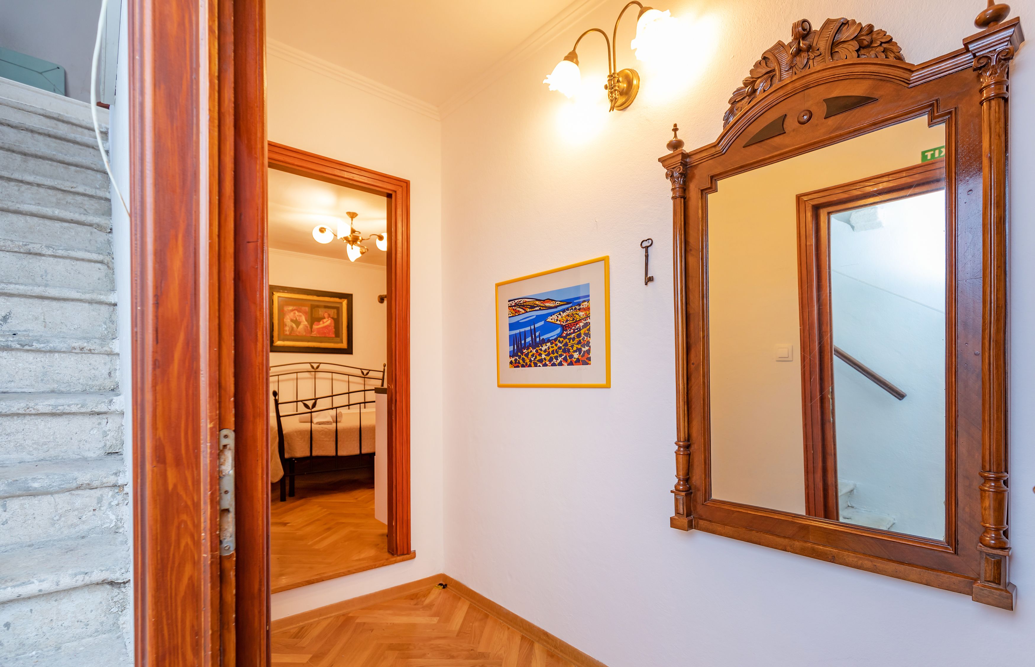 Un pasillo con puerta de madera, un cuadro enmarcado, un espejo grande y una escalera.