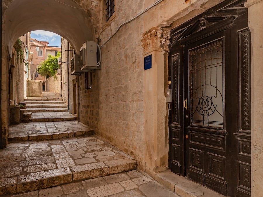 Un estrecho callejón empedrado con una puerta de madera oscura y un arco.