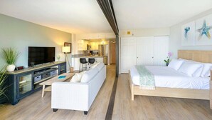 A modern hotel room with a bed, sofa, TV, and kitchenette.