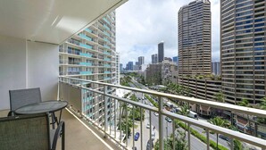 A balcony with a table and chairs, overlooking a cityscape with tall buildings and a busy street.