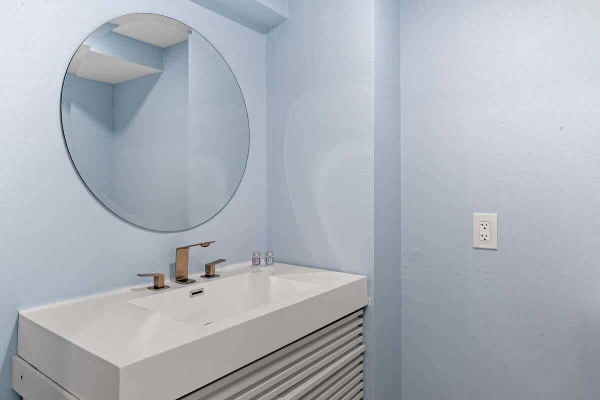 A bathroom with a white sink, a round mirror, and a light blue wall.