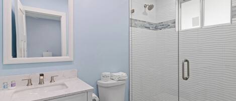 Une salle de bain avec un lavabo en marbre, des toilettes et une douche à l’italienne aux parois texturées.