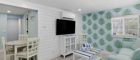 Una sala moderna con comedor, televisor de pantalla plana, un armario blanco y una pared con diseño.