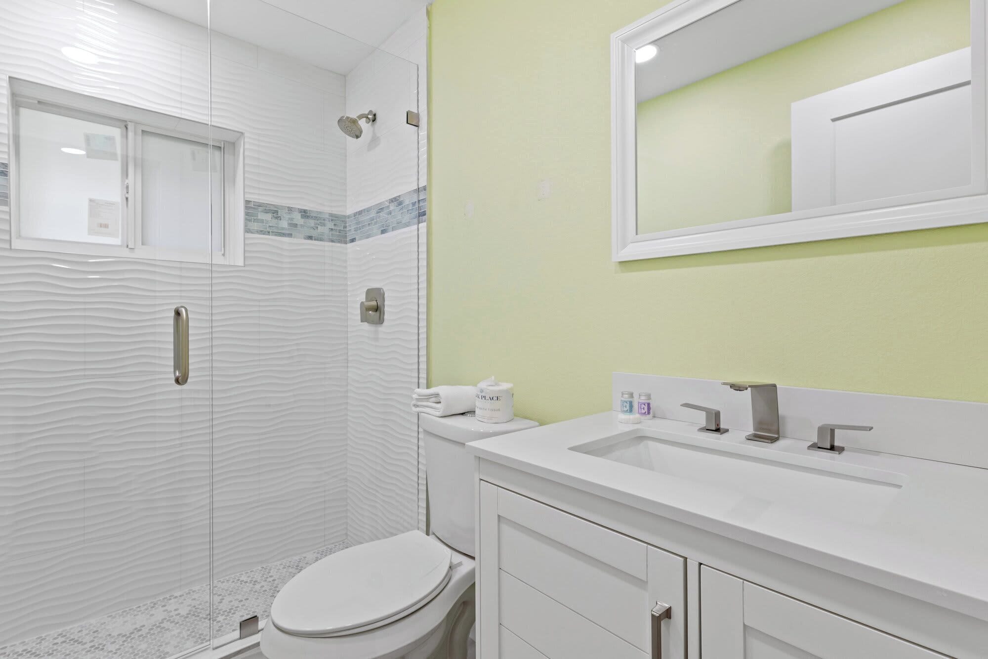 Un baño con ducha, inodoro, lavabo y espejo.