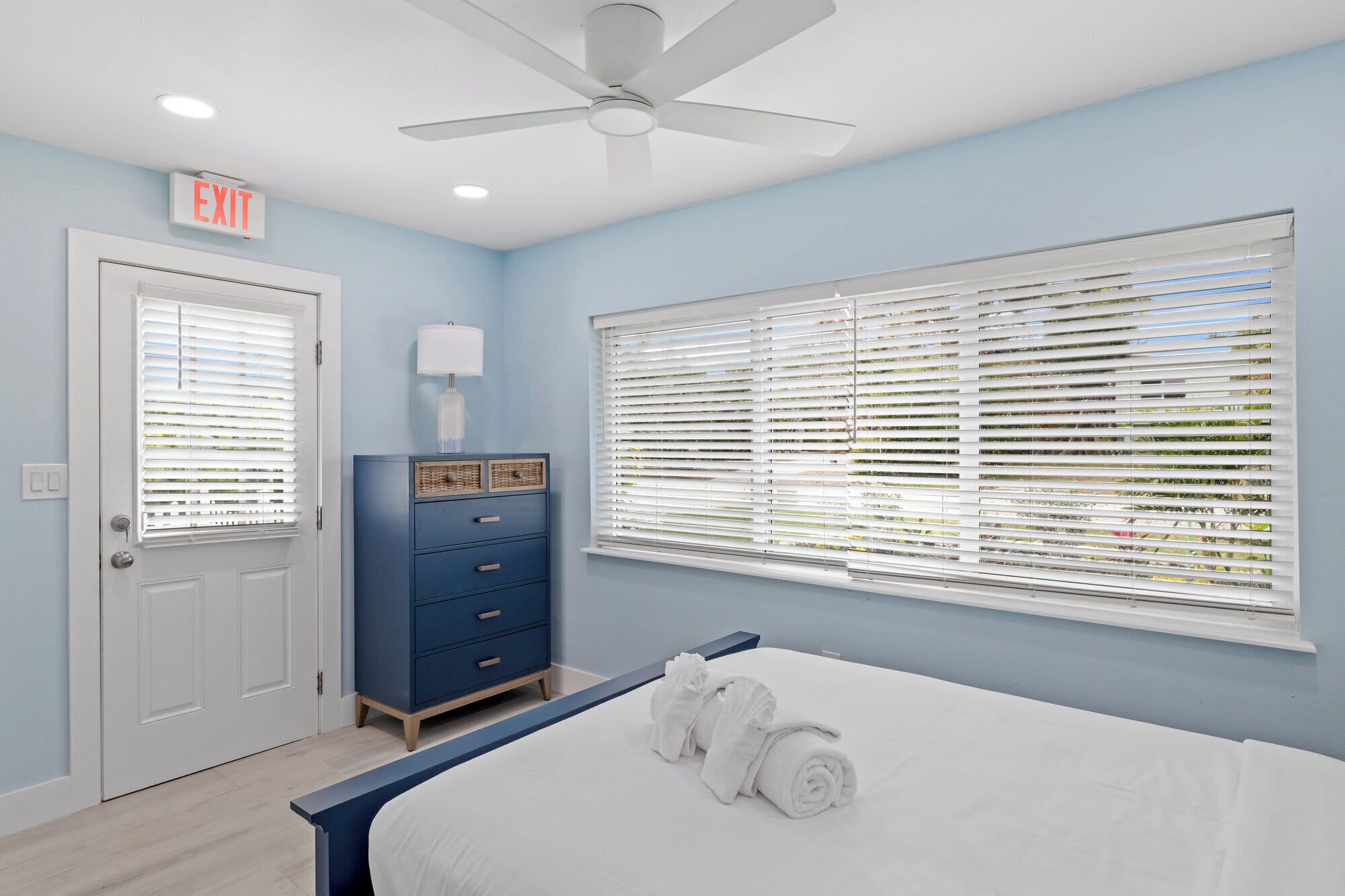 A bedroom with a bed, a dresser, a ceiling fan, and a window with blinds.