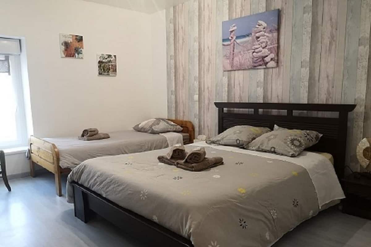 Quarto com duas camas individuais, cabeceira de madeira e uma janela.