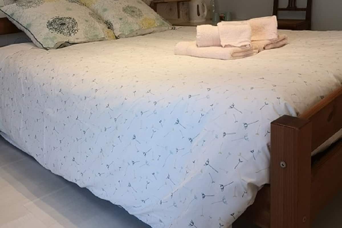Um quarto com cama, travesseiros, mesa de cabeceira, abajur, cadeira e uma prateleira na parede.
