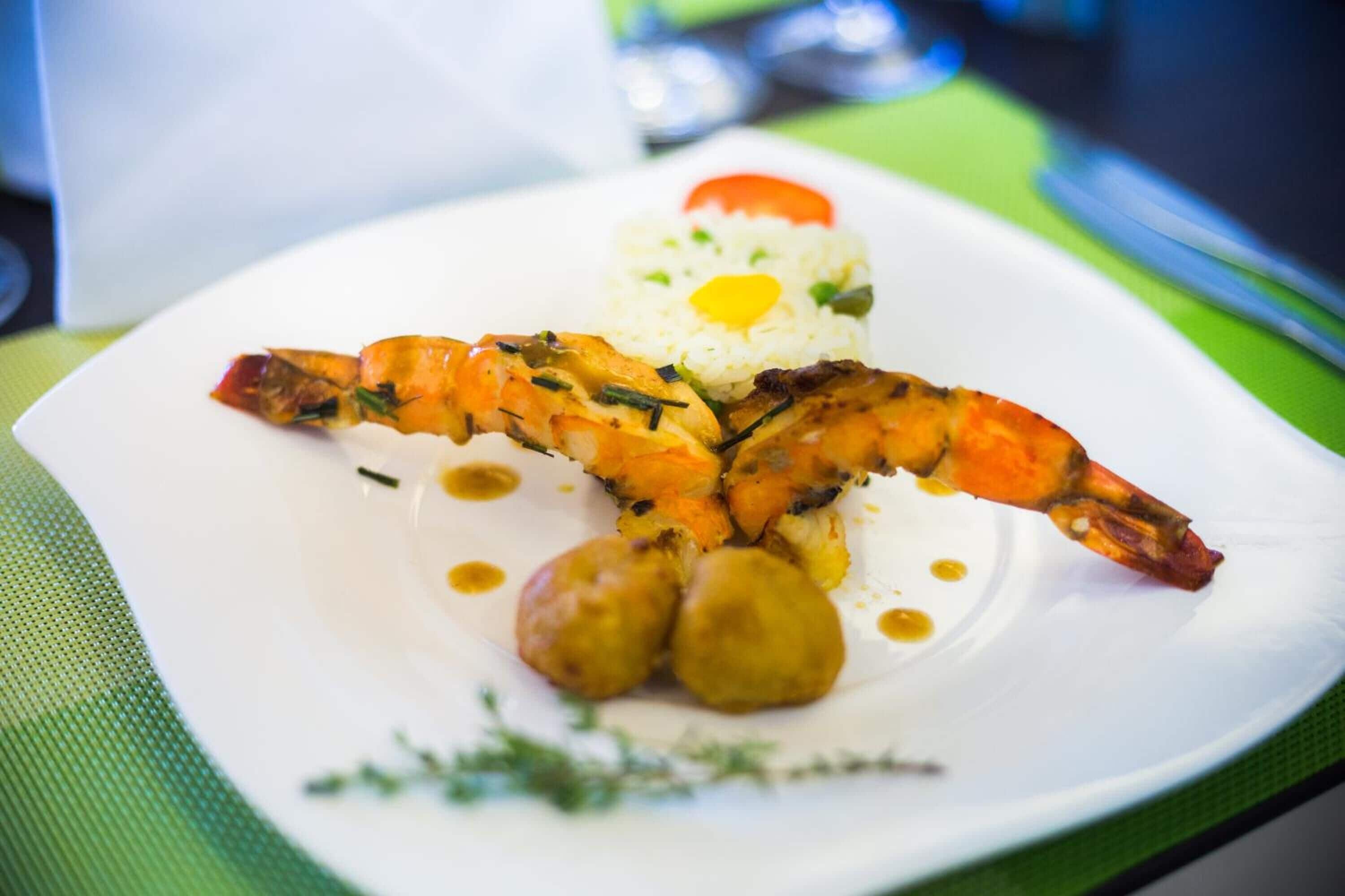 A plate with grilled shrimp, rice, and a tomato on a white plate.