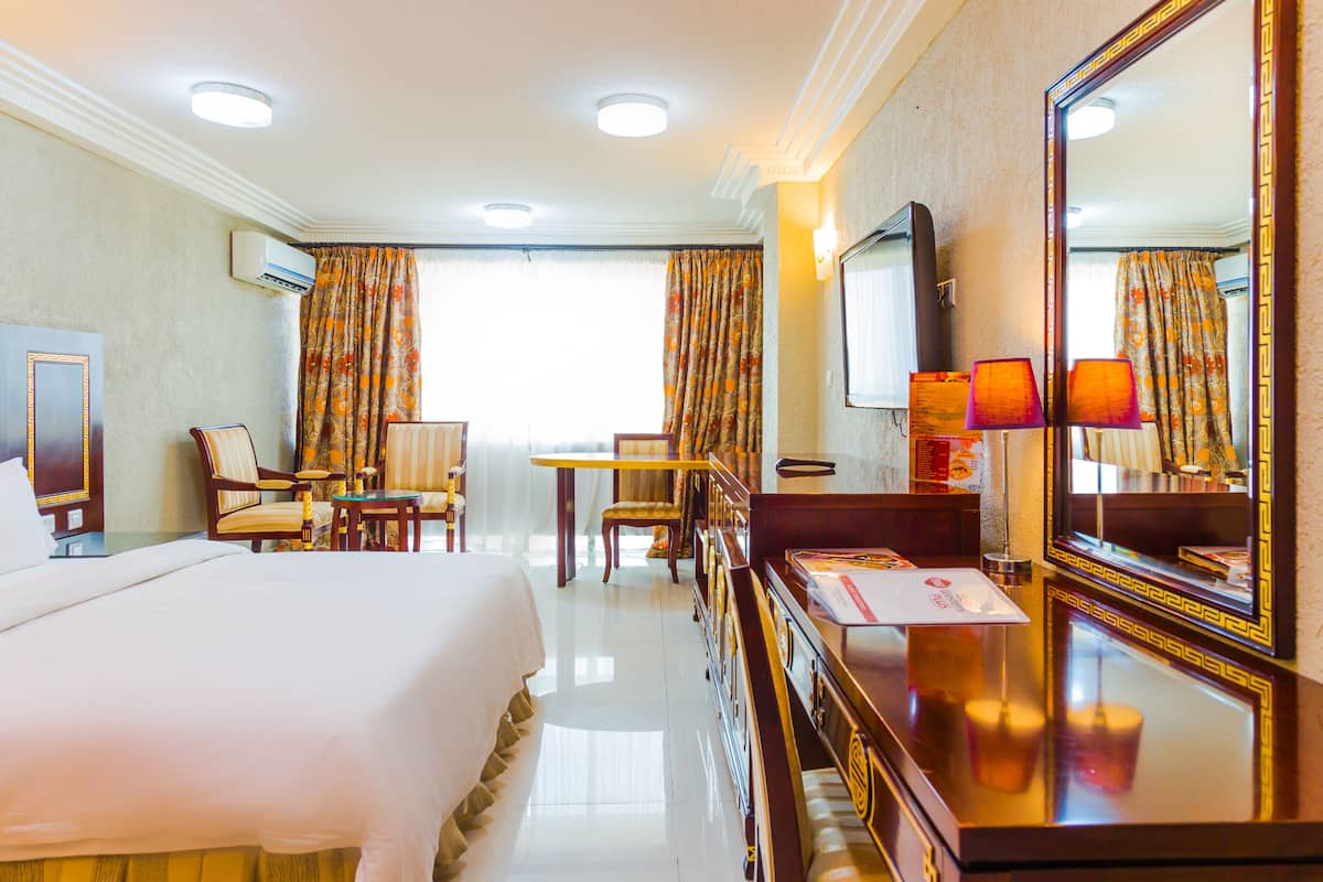 A hotel room with a bed, a desk, a chair, a TV, and a large mirror.