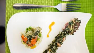 A white plate with a dish of rice and vegetables, and a piece of meat with a green topping.
