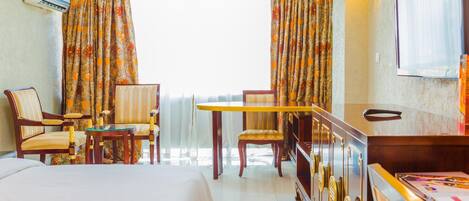 A hotel room with a bed, two chairs, a small table, a minibar, and a television.