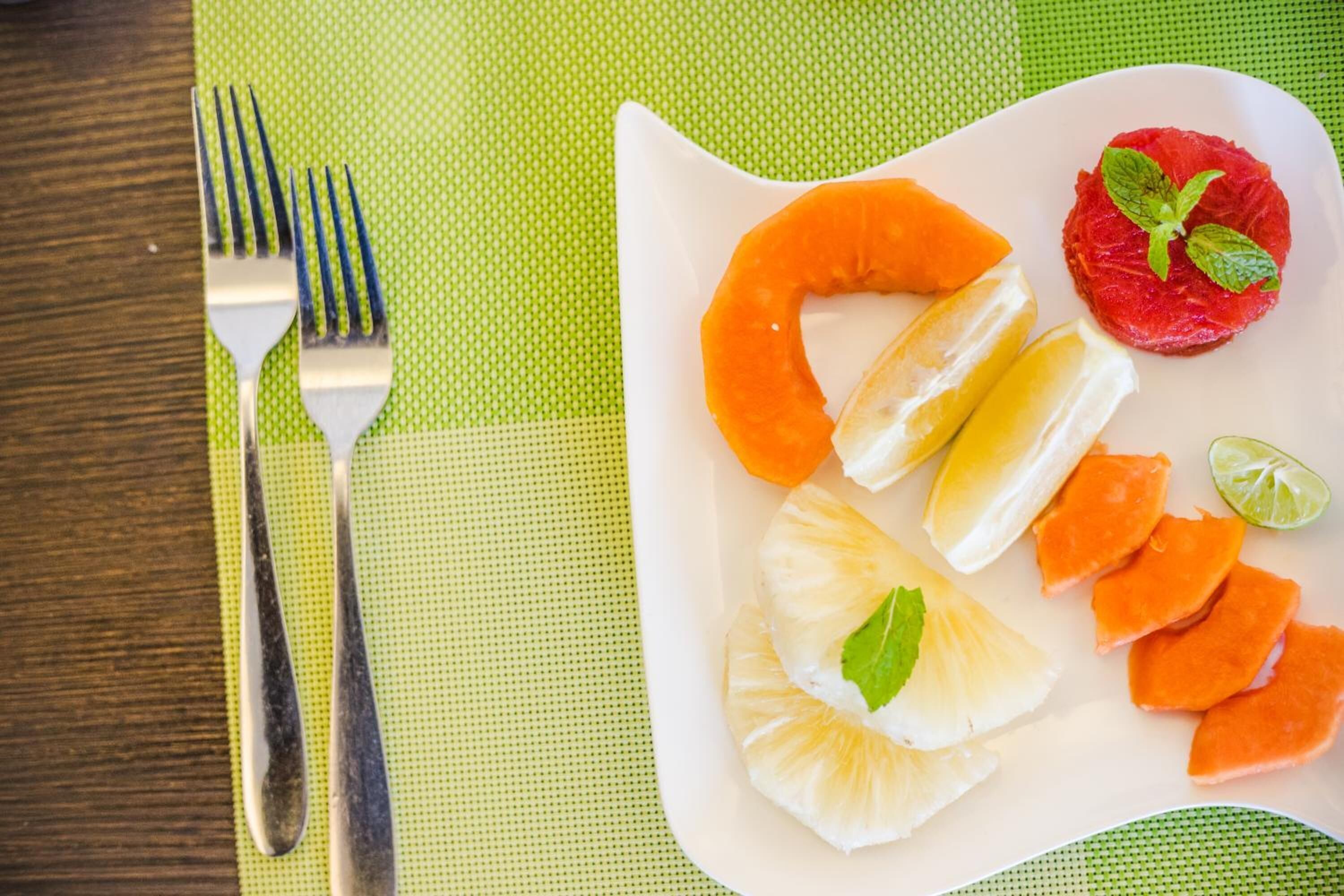 Un plato blanco con frutas cortadas y una ramita de menta sobre una base verde.
