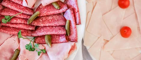 Un plato de embutidos con pepinillos y perejil, y otro plato de jamón con tomates cherry.