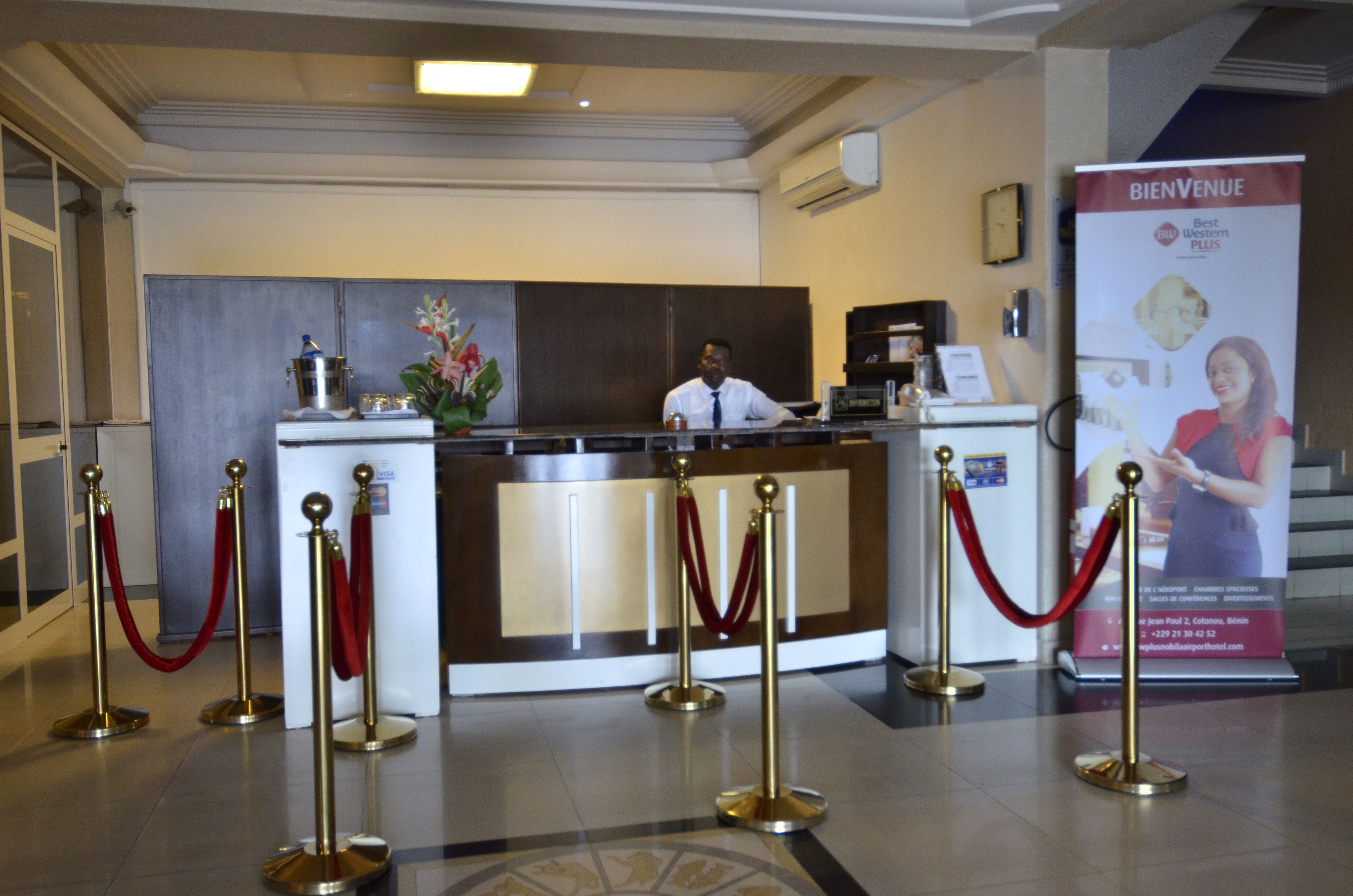 Un hall d’hôtel avec un comptoir d’accueil, un homme derrière le comptoir et une entrée recouverte d’un tapis rouge.