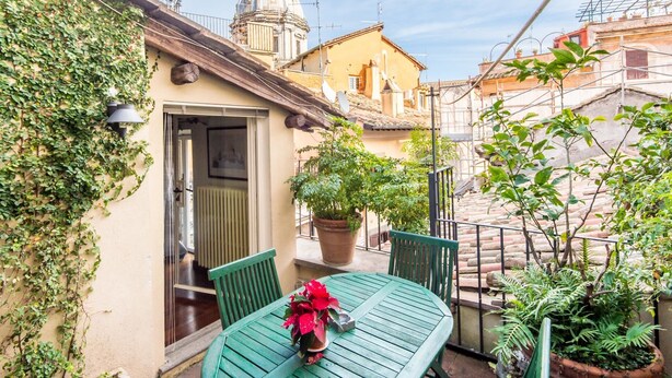 A courtyard with a green table and chairs, potted plants, and a building with a dome. - RSH Campo de Fiori Luxury House (Rome)