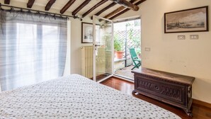 A bedroom with a bed, a wooden dresser, a radiator, and a door leading to a balcony with potted plants. - RSH Campo de Fiori Luxury House (Rome)