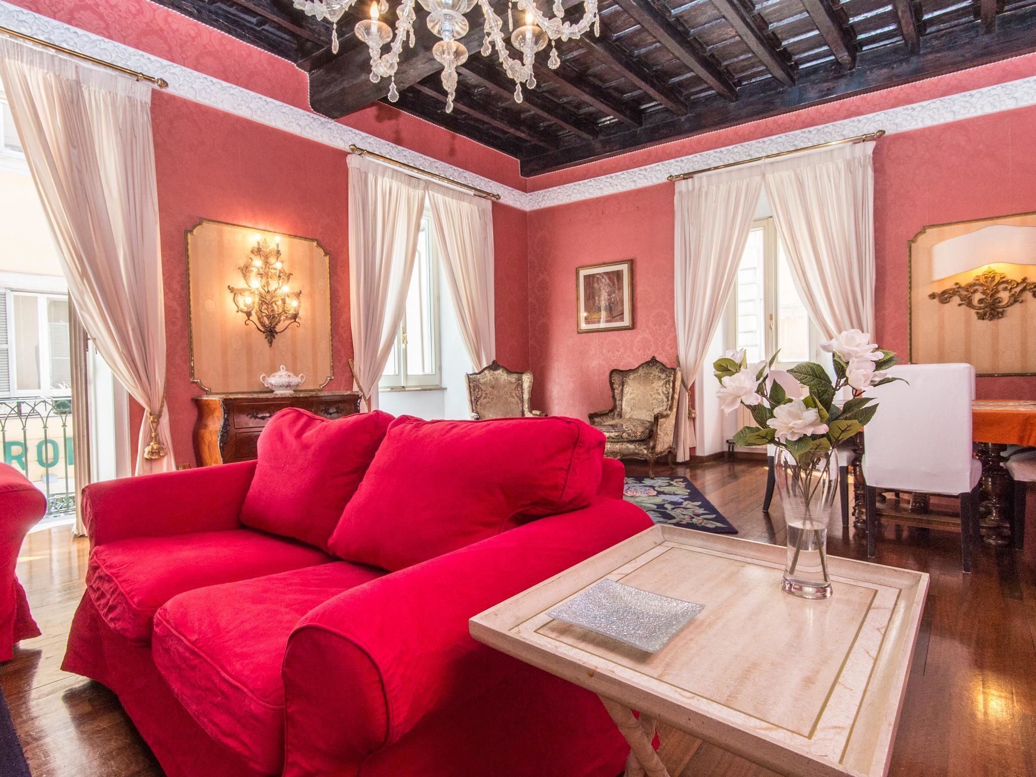 A room with a red sofa, a wooden coffee table, a chandelier, and a dining area with a table and chairs.
