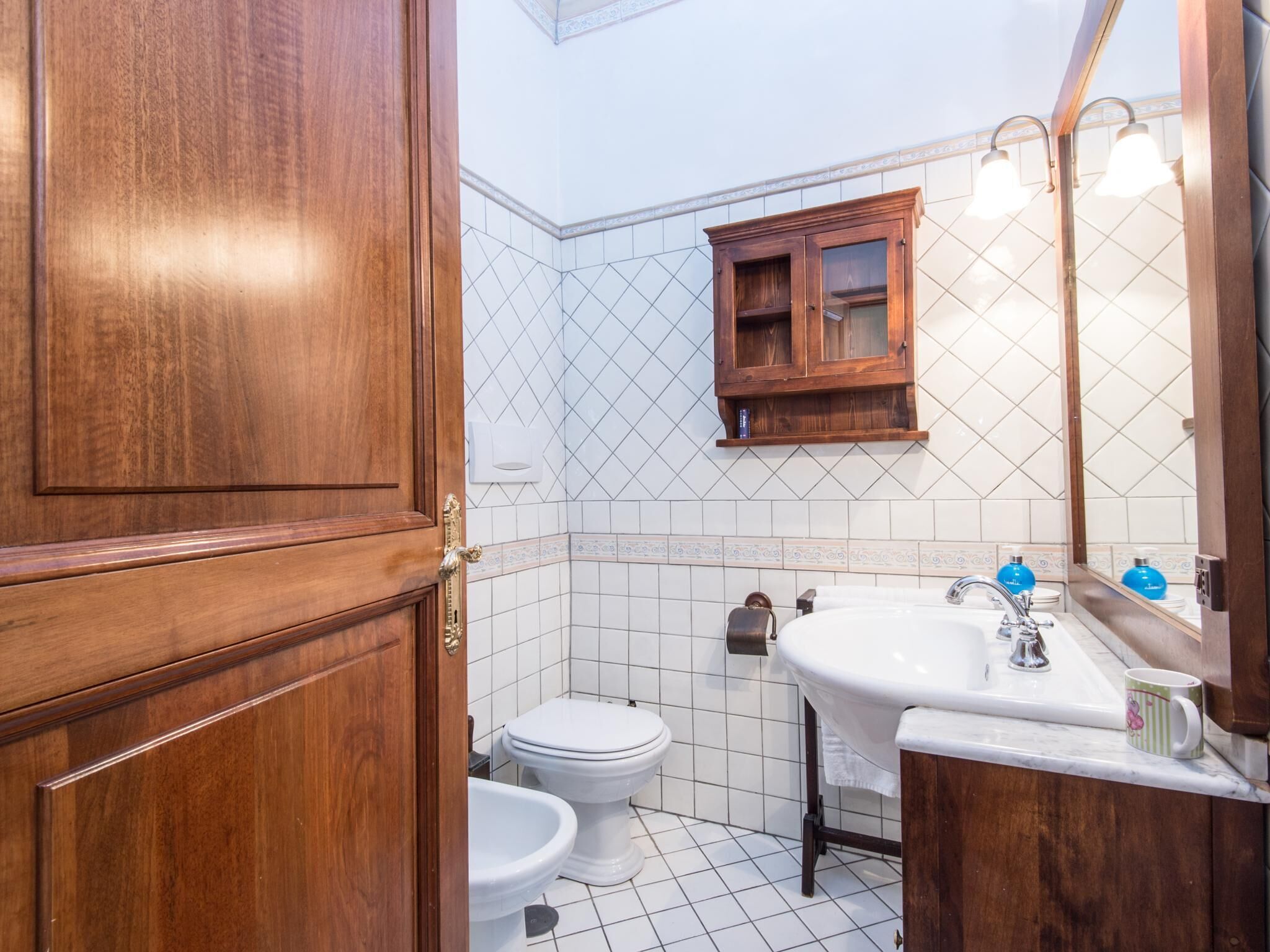 Ein Badezimmer mit Holztür, Toilette, Waschbecken mit Spiegel und einem Schrank darüber.