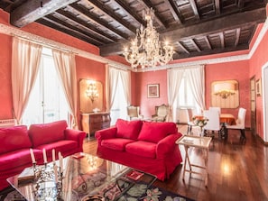 A room with red sofas, a glass coffee table, a chandelier, and a dining area with a table and chairs.