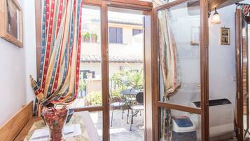 Una habitación con una mesa de madera, un florero con flores secas y una ventana con cortinas.