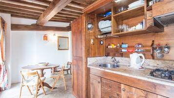 Una cocina rústica con gabinetes de madera, un fregadero y una estufa. Hay una mesa de comedor con sillas y una lámpara colgante.