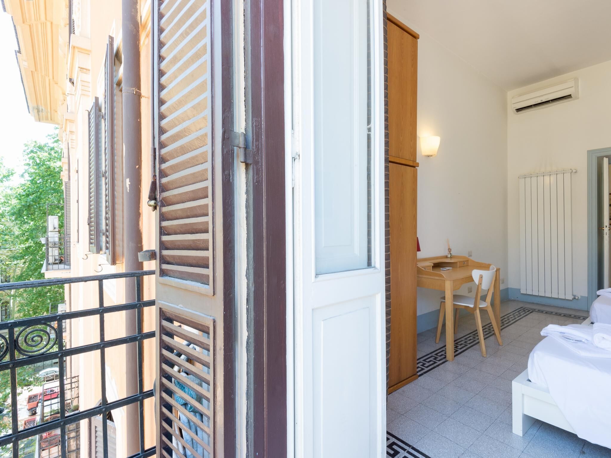 Een hotelkamer met balkon, een houten bureau, een stoel, een bed en een radiator.