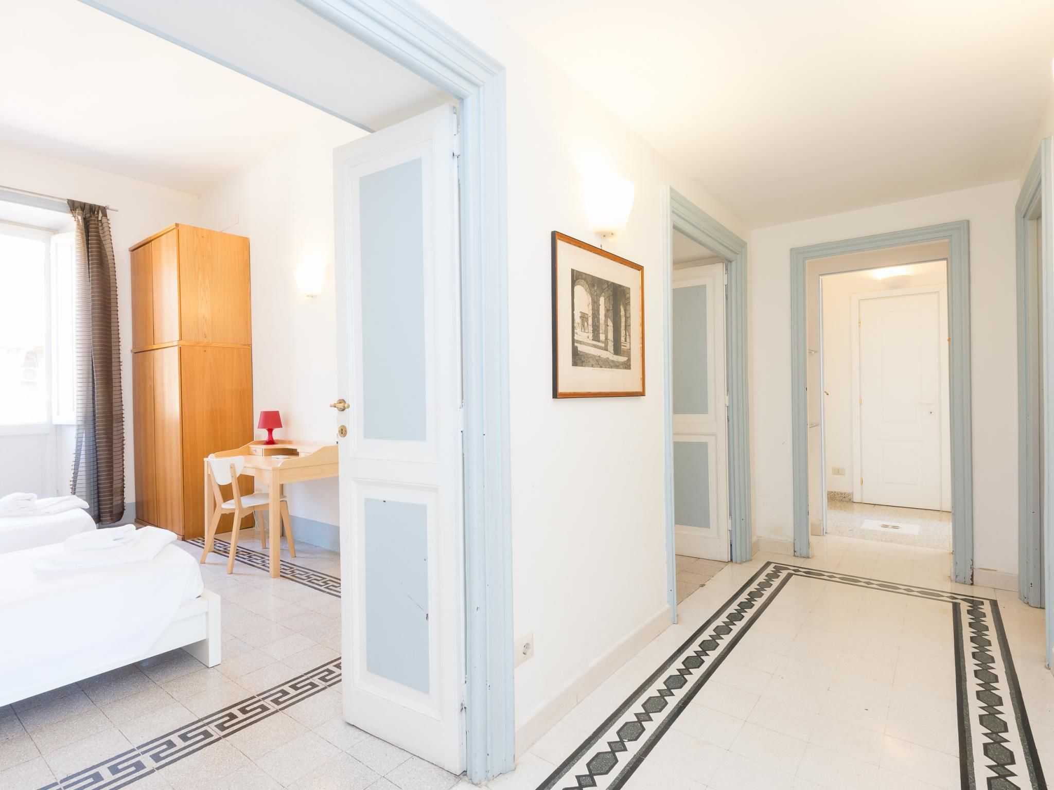 A hotel room with a bed, a desk, and a chair. There is a door leading to another room.