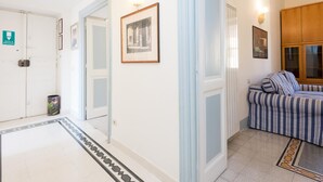 Un couloir avec une porte blanche portant l’inscription « SORTIE DE SECOURS », un tableau encadré et un canapé à rayures.