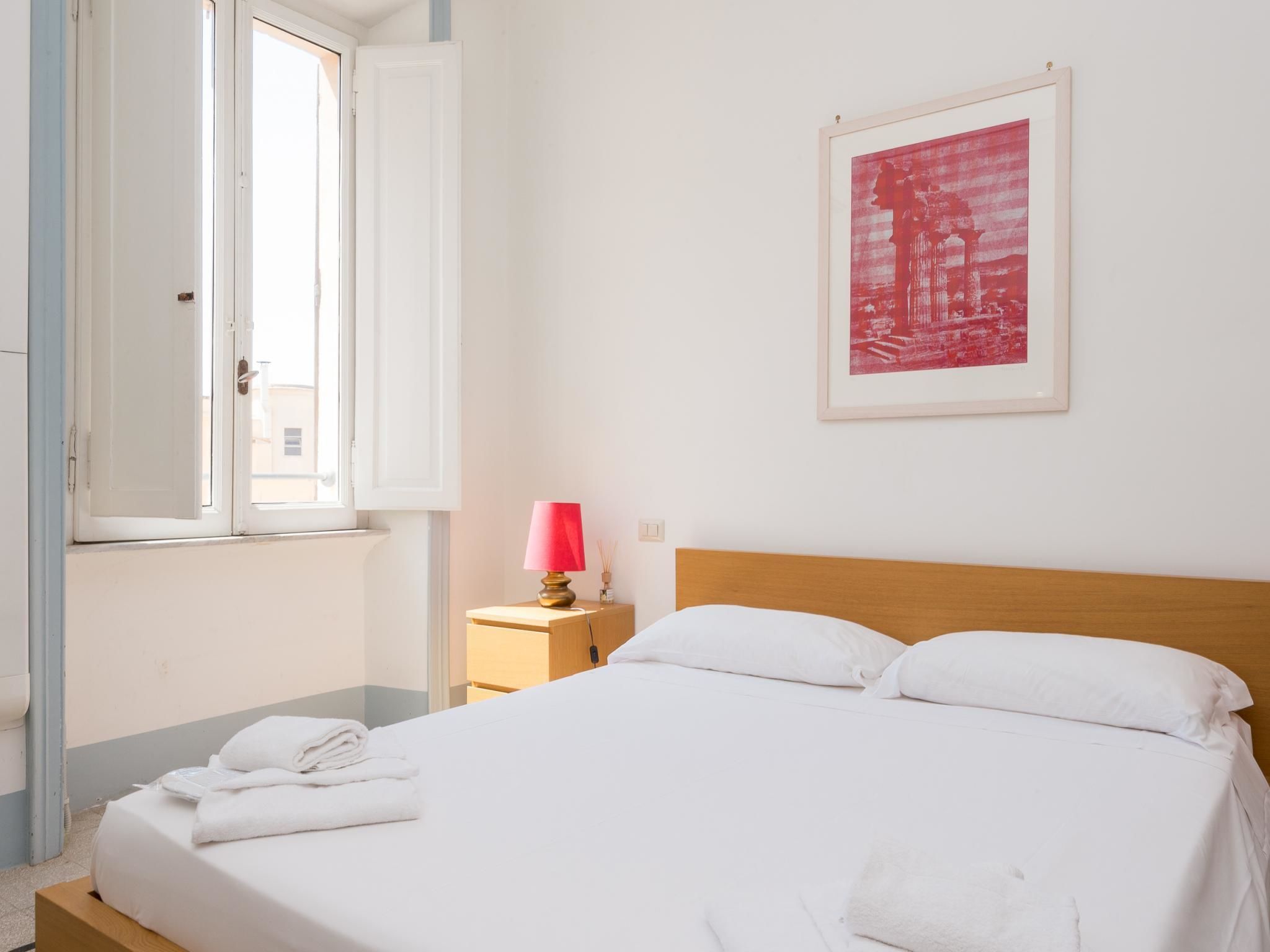 A neatly made bed with white linens, a wooden headboard, and a pink lamp on a bedside table.