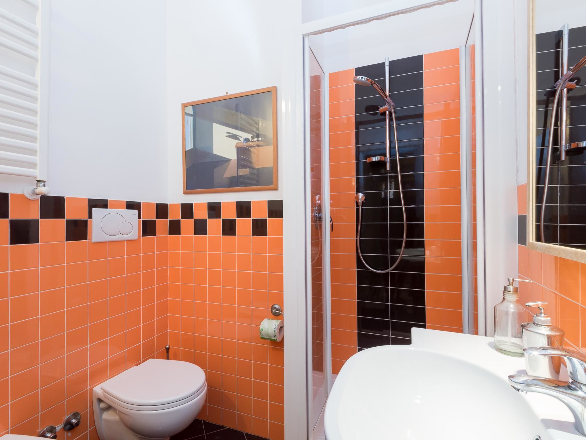 A bathroom with orange and black tiles, a white toilet, a shower with a glass door, and a sink with a mirror.