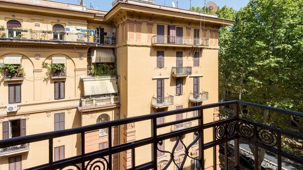 Un immeuble à plusieurs étages doté de balcons, dont certains sont ornés de plantes, et un ciel dégagé.
