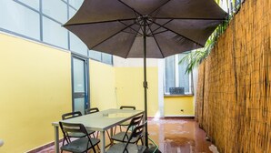 A room with a table and chairs, a large umbrella, a bamboo wall, and a window. - RSH Ara Pacis Terrace Apartment (Rome)