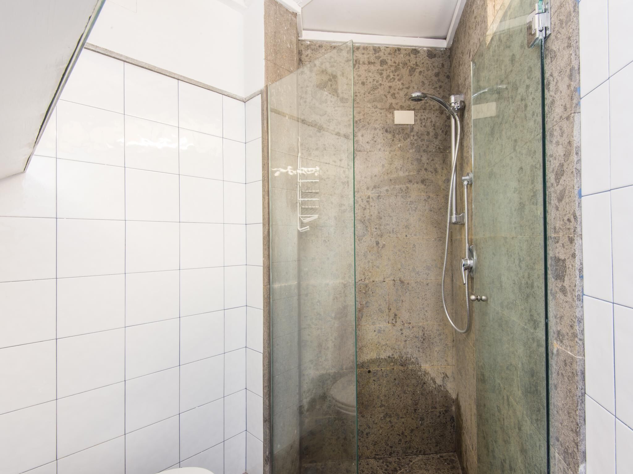 A modern bathroom with white tiles, a glass shower enclosure, and a marble shower wall.
