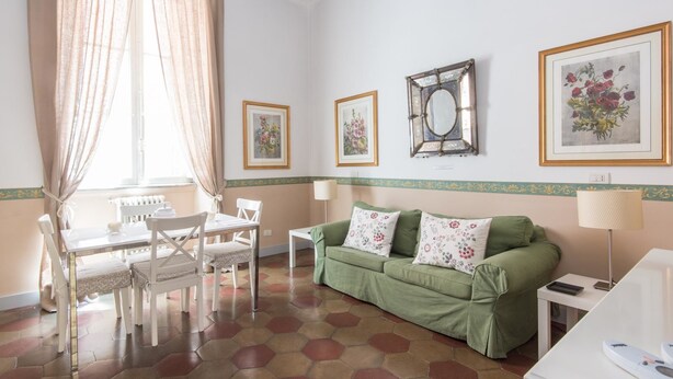 A room with a green sofa, white chairs, a dining table, and hexagonal patterned flooring. - RSH Ara Pacis Terrace Apartment (Rome)