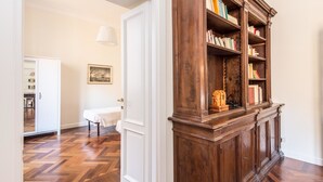 Ein Zimmer mit Fischgrat-Holzboden, einer weißen Tür, einem weißen Tisch mit weißem Tischlein und einer hölzernen Bücherwand voller Bücher.