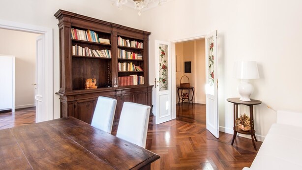 Ein geräumiges Zimmer mit einem Holzespeisesaal, zwei weißen Stühlen, einer großen Holzbibliothek und einer Chandelier.