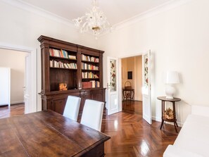 Ein geräumiges Zimmer mit einem Holzespeisesaal, zwei weißen Stühlen, einer großen Holzbibliothek und einer Chandelier.