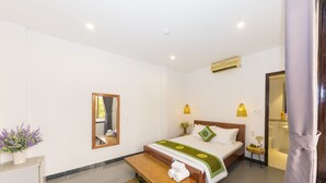 Quarto de hotel com cama, mesa de cabeceira, banqueta, espelho e uma pequena mesa com uma planta.