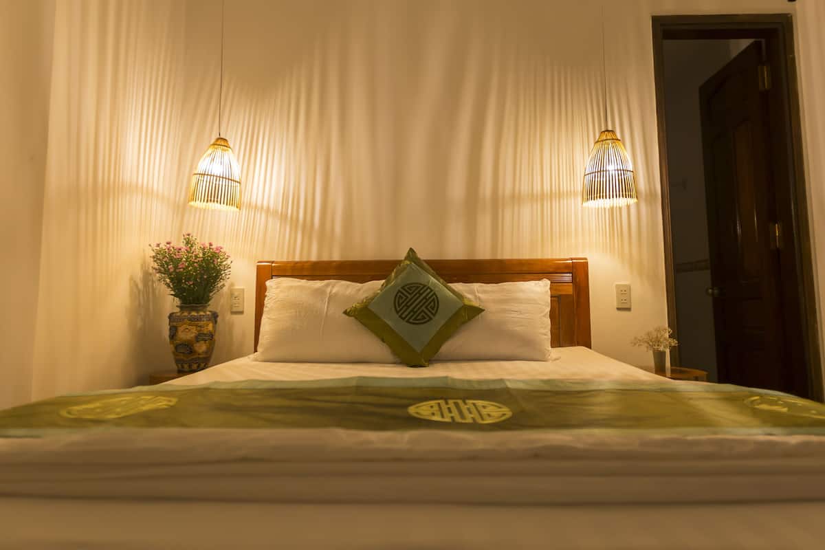 A neatly made bed with a green and white bedspread, two bedside lamps, and a vase with flowers on the nightstand.