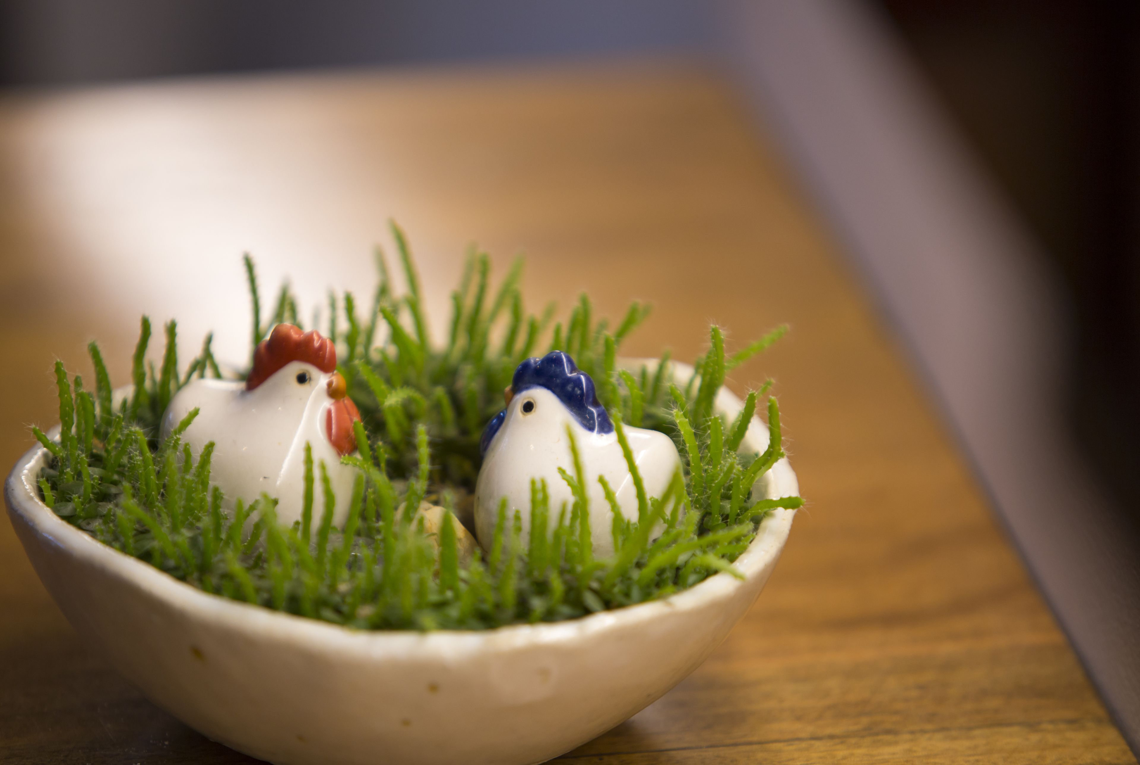 A ceramic bowl with two figurines of chickens on a wooden surface.
