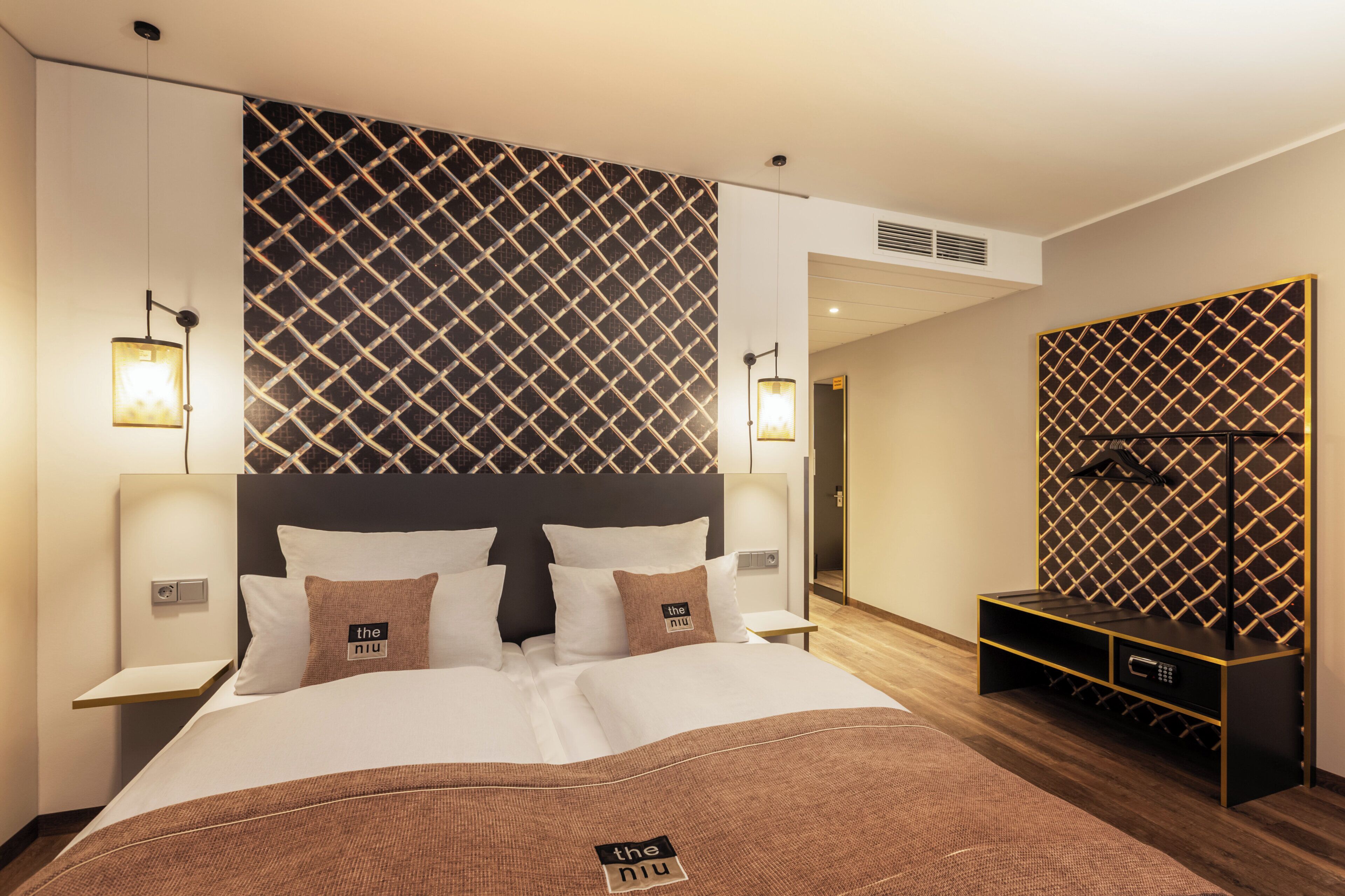 Ein modernes Hotelzimmer mit einem großen Bett, zwei Nachttischen, einem integrierten Fernseher und einer Minibar.