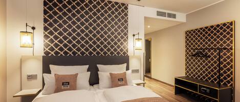Una habitación de hotel moderna con una cama grande, dos mesitas de noche, un televisor integrado y un minibar.