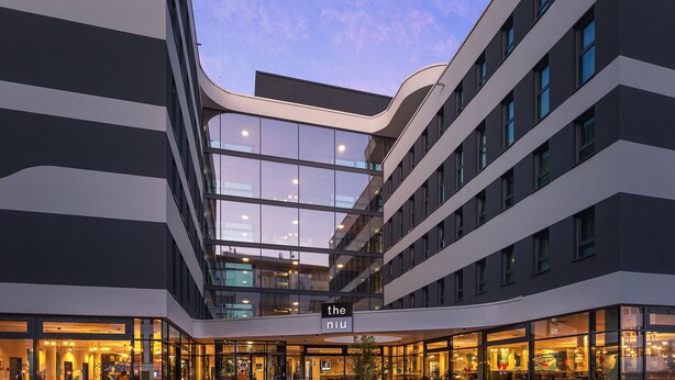 Un edificio moderno con fachada de vidrio y varios pisos, y un letrero que dice "the niu".