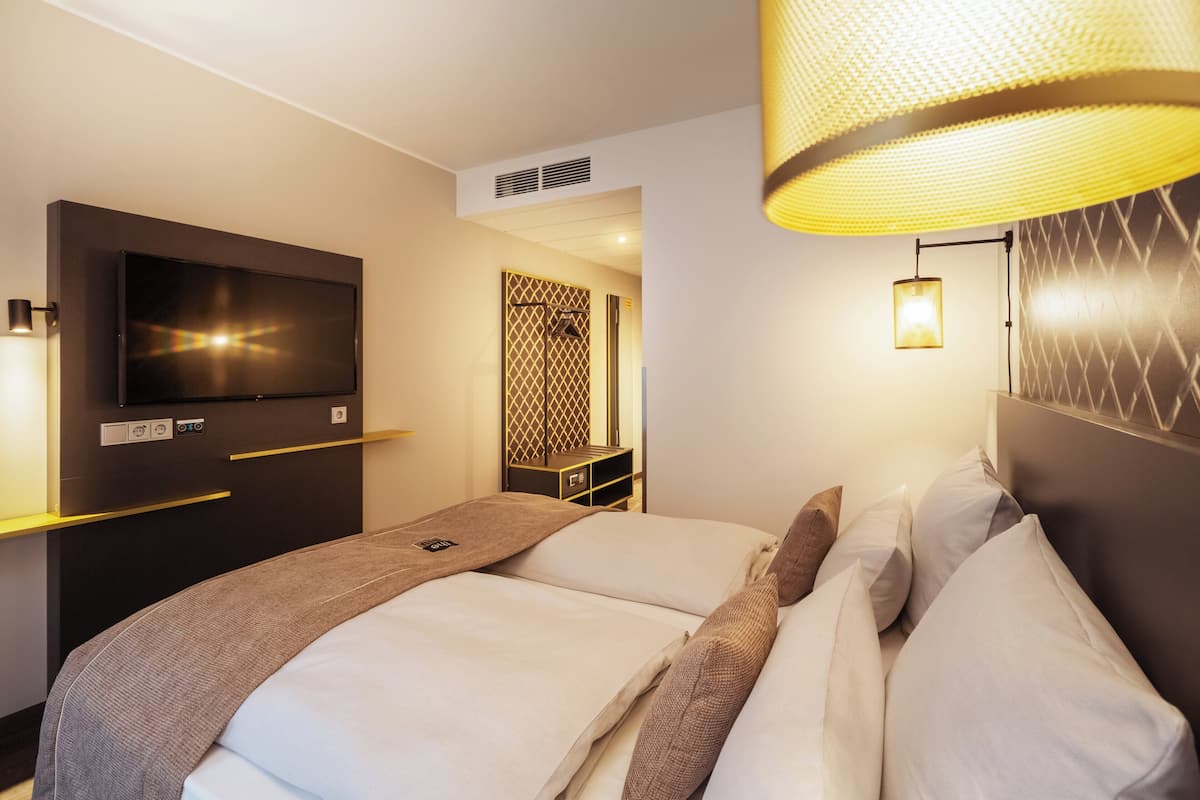 A hotel room with a large bed, a flat-screen TV, a wall-mounted TV, and a modern lamp.