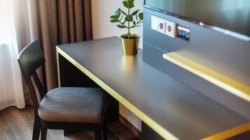 Una habitación de hotel moderna con piso de madera, una silla marrón oscuro, una pequeña planta en maceta y un televisor de pantalla plana sobre un pedestal de madera.