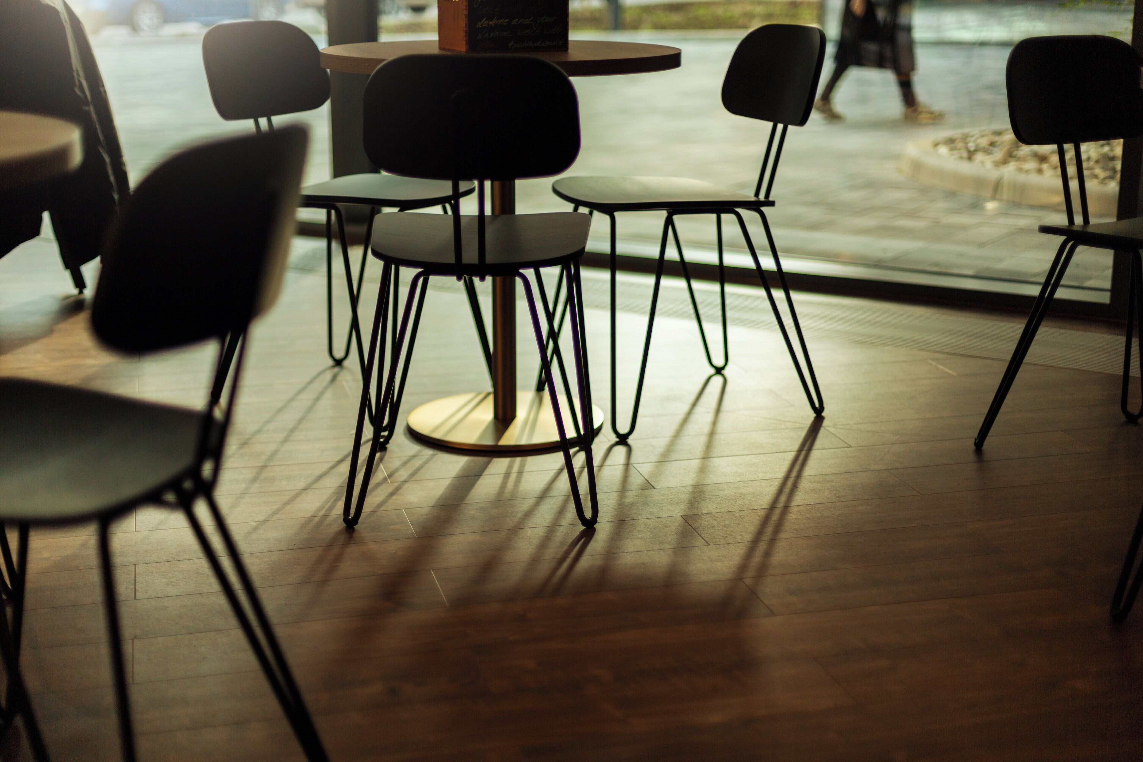 Un intérieur moderne avec des tables rondes et des chaises noires, un plancher en bois et une vue sur l’extérieur.
