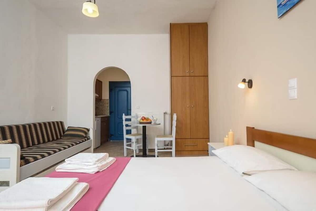 Quarto de hotel com cama, sofá, escrivaninha com cadeira, armário e uma pequena mesa com frutas.